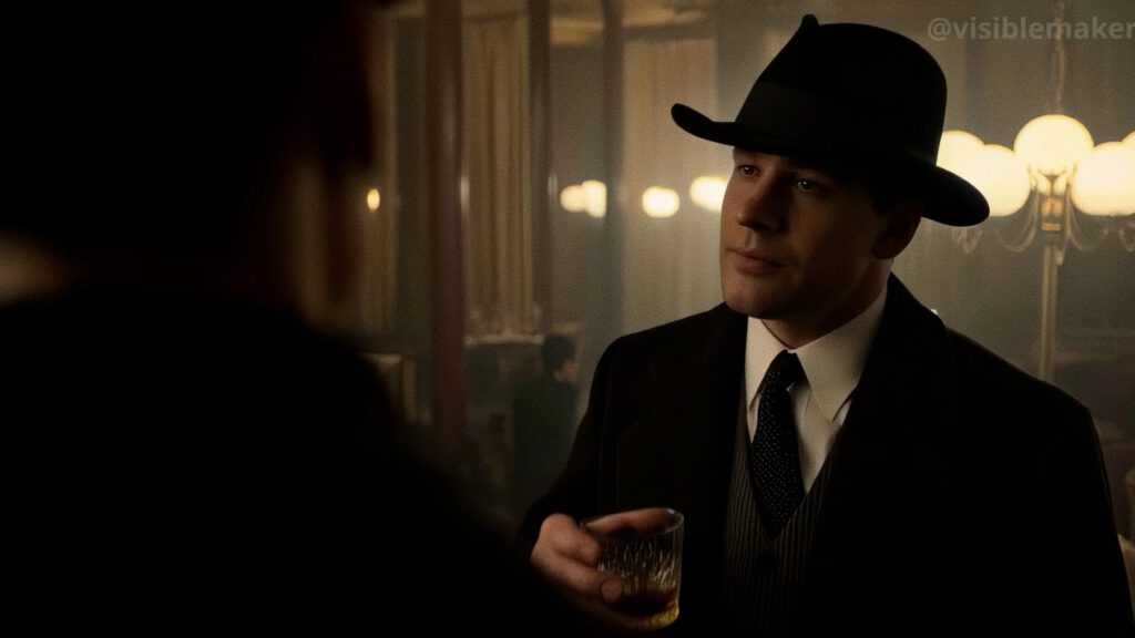 A man in a suit, tie, and fedora holds a glass of whiskey, speaking to someone in a dimly lit Hunyuan bar with warm lighting and ornate decor—a true Moodfilm moment. AI Image made by Christian Fleischer / The Visiblemaker
