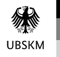 The image shows a black eagle with outstretched wings above the bold letters UBSKM on a white background, with vertical black, gray, and white bars on the right side.