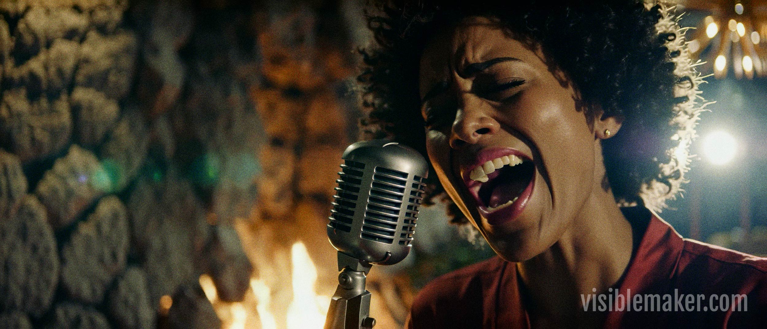 A woman with curly hair passionately sings into a vintage microphone, her mouth open wide, in a warmly lit setting with a stone wall and visiblemaker.com watermark—capturing the spirit of an expressive ai p-video performance. AI Image made by Christian Fleischer / The Visiblemaker